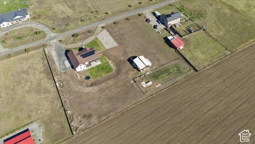 Aerial view of a multi-structure property featuring a primary residence with solar panel arrays, a detached auxiliary structure, gravel driveways, and expansive open acreage