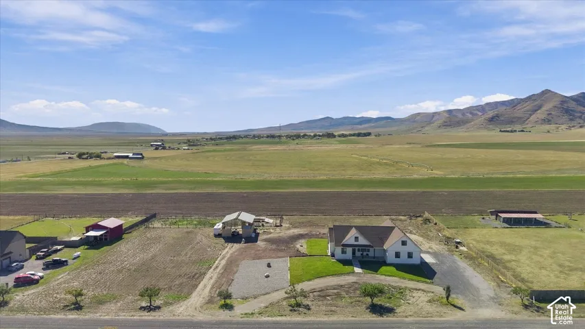 Aerial perspective featuring an expansive lot with a single-story residence, a detached storage structure, an open-sided carport, and mountain topography