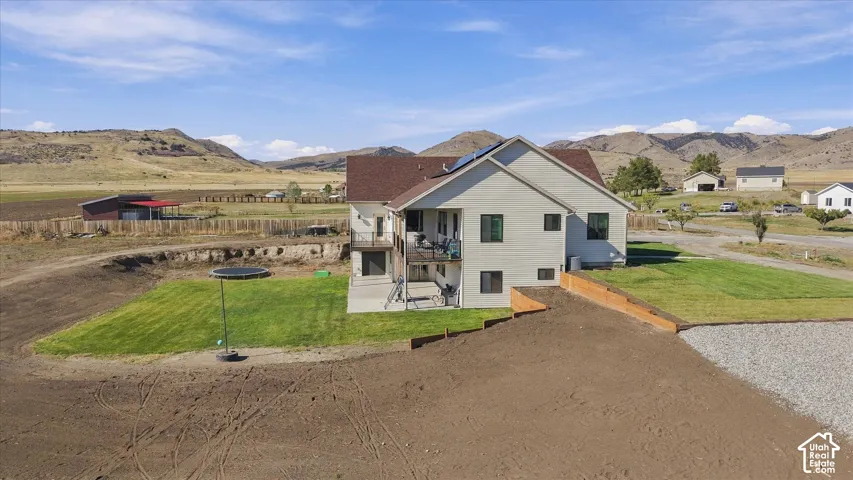 Two-story residence featuring composite siding, a roof-mounted solar array, a multi-level deck, concrete patio, and landscaped lawn areas