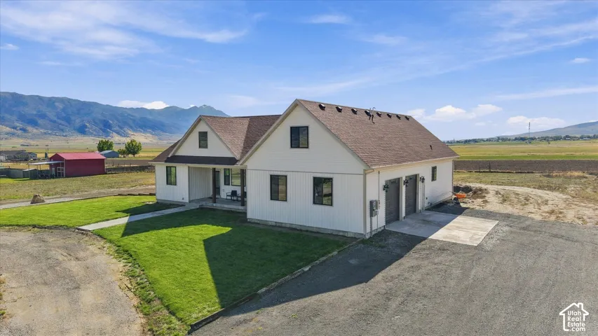 Board-and-batten exterior with an attached two-car garage, multi-gabled shingled roof, mountain backdrop, and manicured lawn