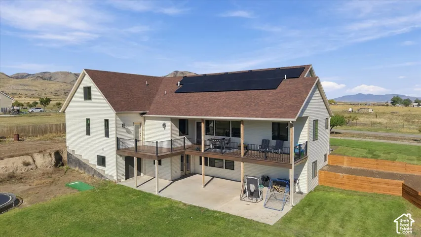 Multi-level exterior featuring solar panel array, elevated deck with metal railing, and covered concrete patio