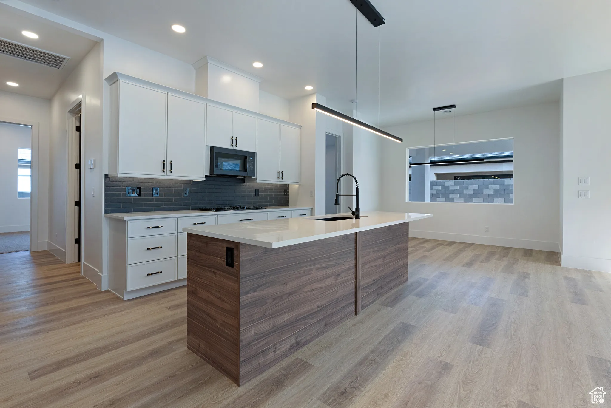 Kitchen with light wood-style floors, light countertops, an island with sink, backsplash, and white cabinetry