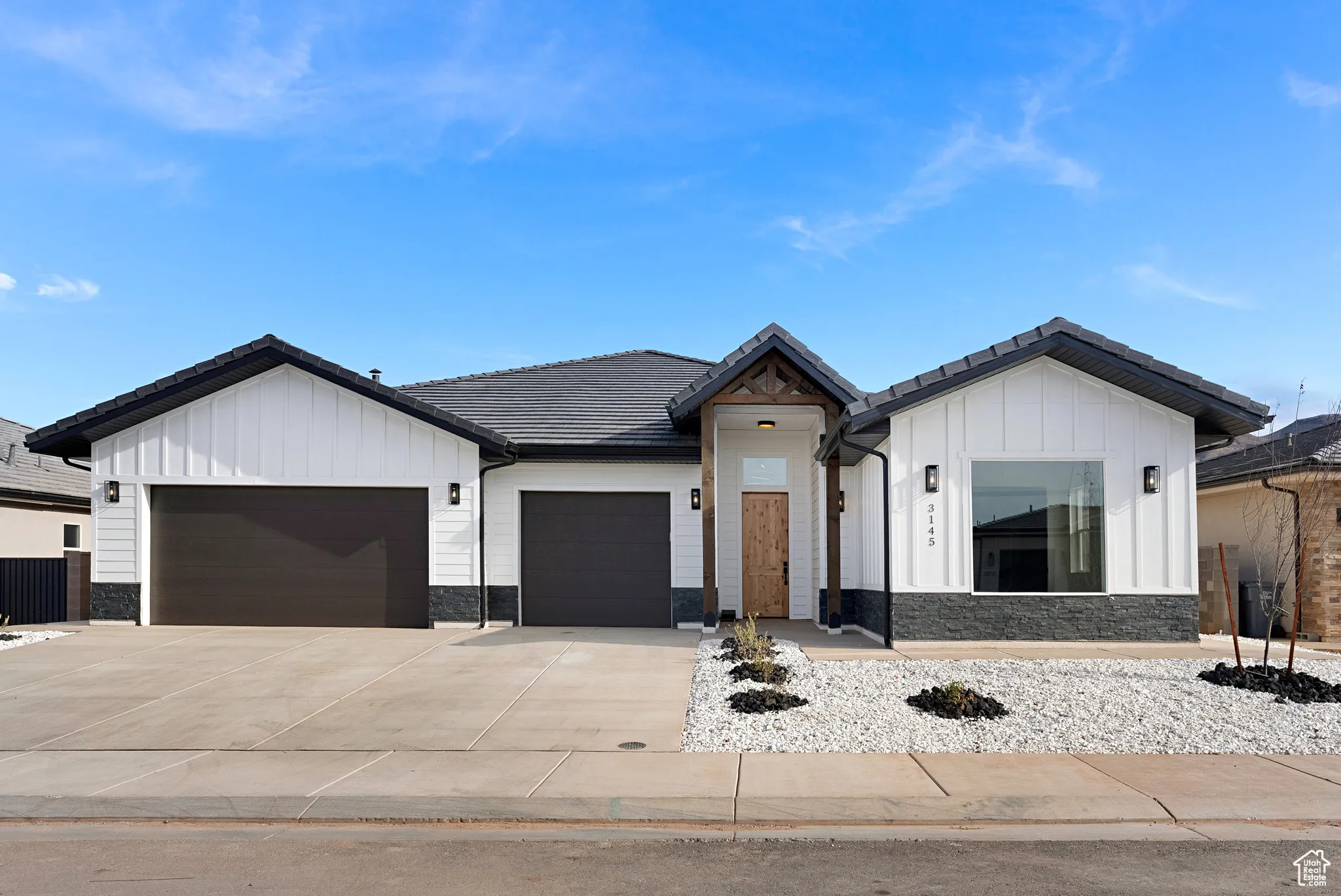 Modern inspired farmhouse with board and batten siding, a garage, stone siding, a tiled roof, and driveway