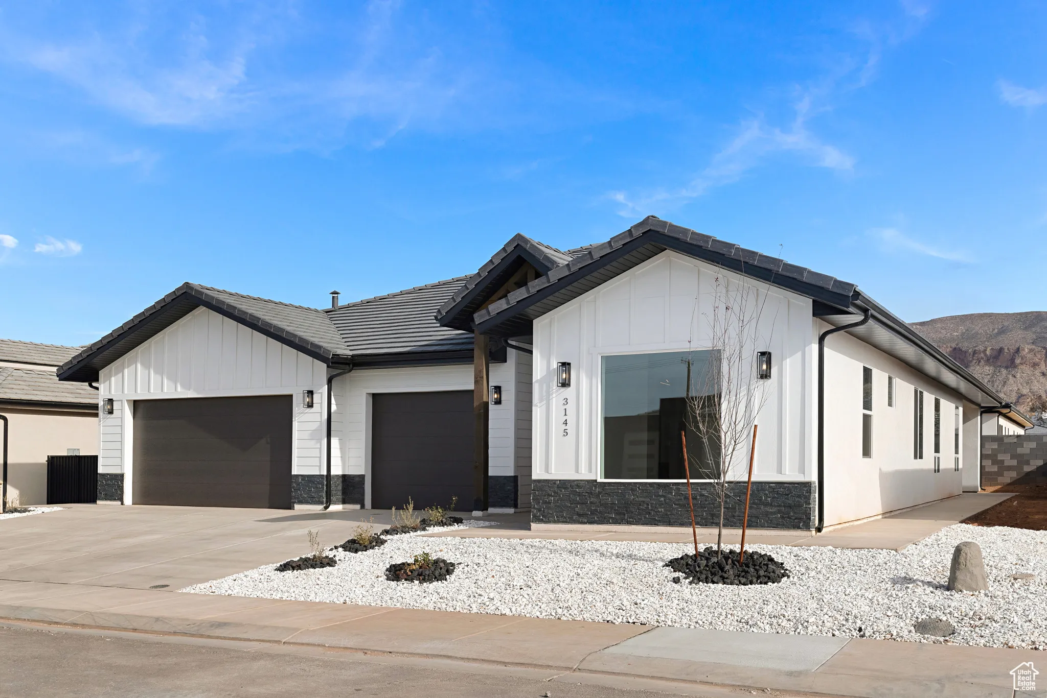 Modern farmhouse with an attached garage, stone siding, driveway, board and batten siding, and a tile roof