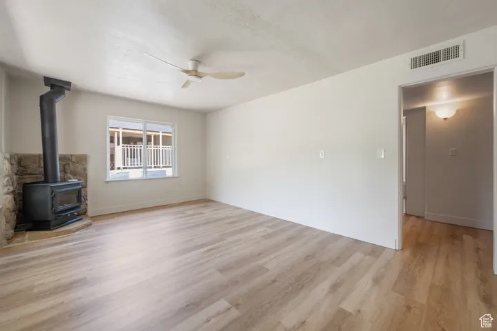 Unfurnished living room featuring a ceiling fan, a wood stove, and light wood-type flooring