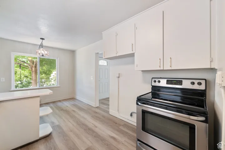 Kitchen featuring electric stove, white cabinetry, light wood finished floors, a chandelier, and light countertops