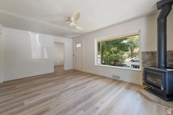 Unfurnished living room featuring a wood stove, wood finished floors, and ceiling fan