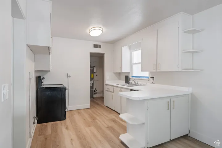 Kitchen featuring open shelves, electric range oven, light countertops, light wood finished floors, and a peninsula