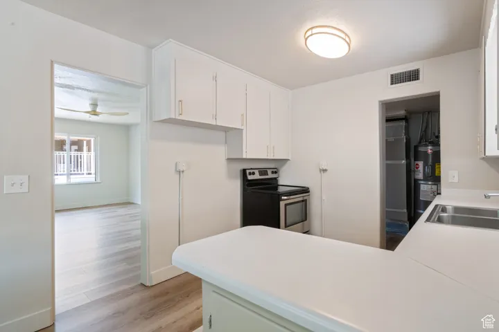 Kitchen with stainless steel electric range oven, light wood finished floors, white cabinets, a peninsula, and light countertops