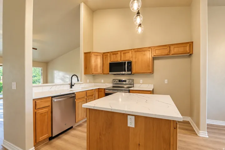 Kitchen featuring light wood cabinetry, stainless steel appliances, white countertops, and wood-finish flooring