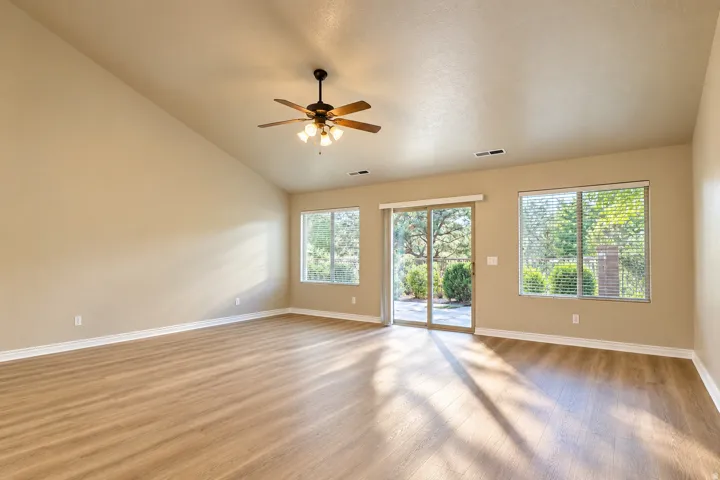 Vaulted ceiling featuring a ceiling fan with integrated lighting, wood-finish flooring, and multiple windows