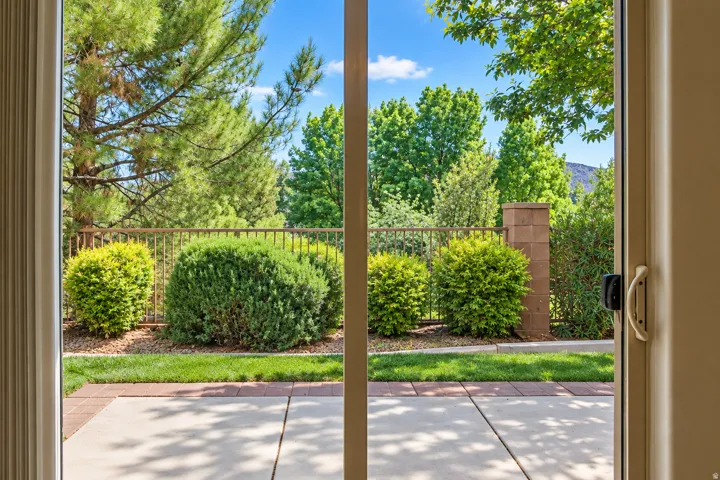 Patio with concrete and brick paver accents, framed by mature shrubs and a metal fence