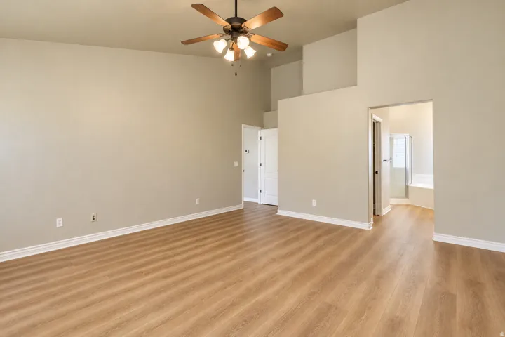 Vaulted ceilings, wood-finish flooring, ceiling fan with light fixture, and an en-suite bathroom featuring a built-in tub with shower
