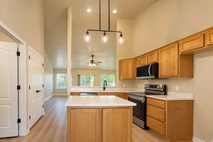 Kitchen featuring a central island, light wood-finish cabinetry, stainless steel appliances, and a modern light fixture