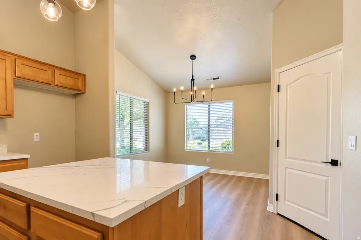 Vaulted ceilings, wood-finish flooring, white countertops, wood cabinetry, and a contemporary chandelier