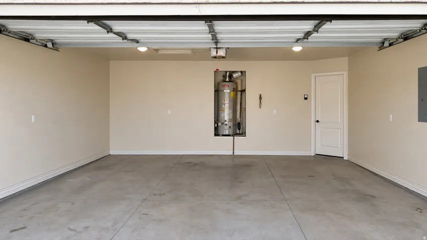 Concrete flooring, recessed water heater, white paneled door, flush-mount lighting, wall-mounted electrical panel
