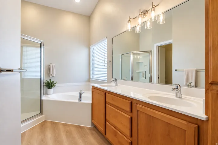 Bathroom featuring a spacious double vanity with wood cabinetry, a large built-in mirror, an enclosed shower, a corner soaking tub, and wood-finish flooring