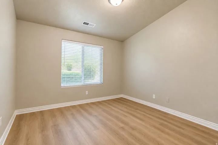 Wood-finish flooring with white trim and a single window featuring blinds