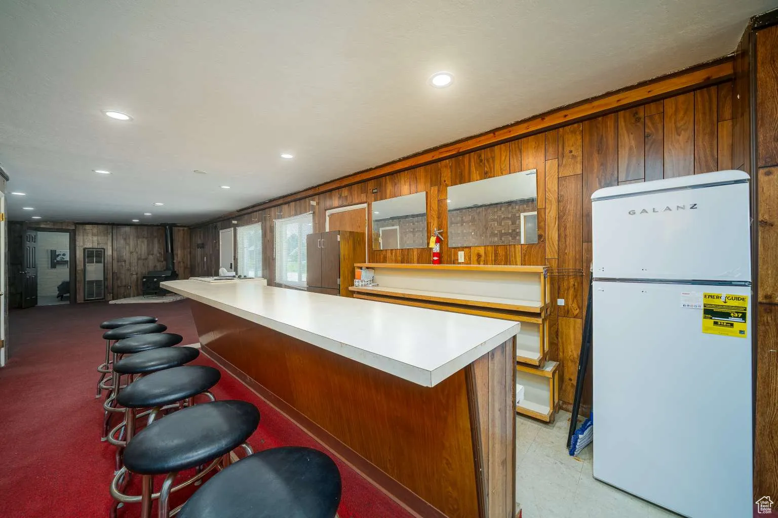 Kitchen featuring freestanding refrigerator, wood walls, light countertops, a breakfast bar, and recessed lighting