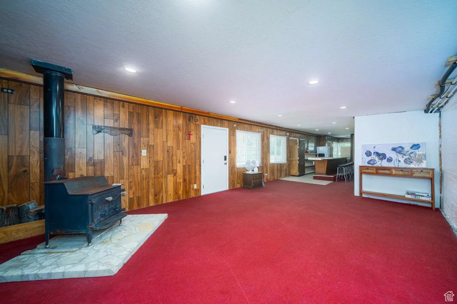 Carpeted living room with a wood stove, wood walls, and recessed lighting