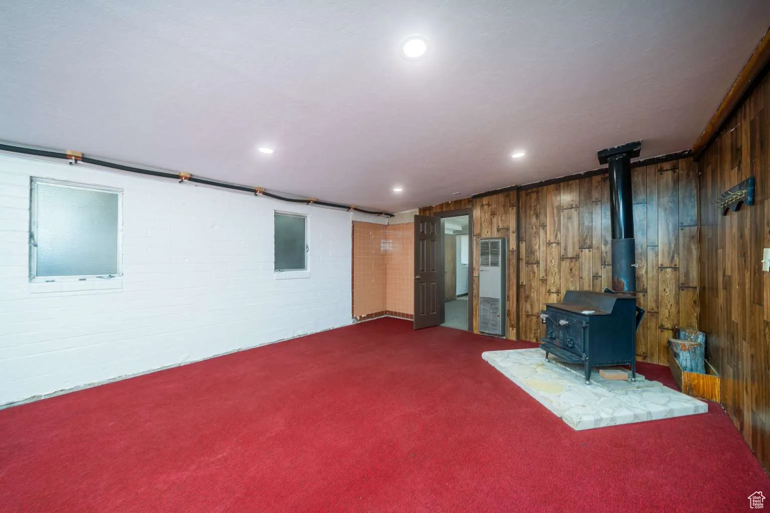 Below grade area with carpet flooring, wood walls, a wood stove, a heating unit, and recessed lighting