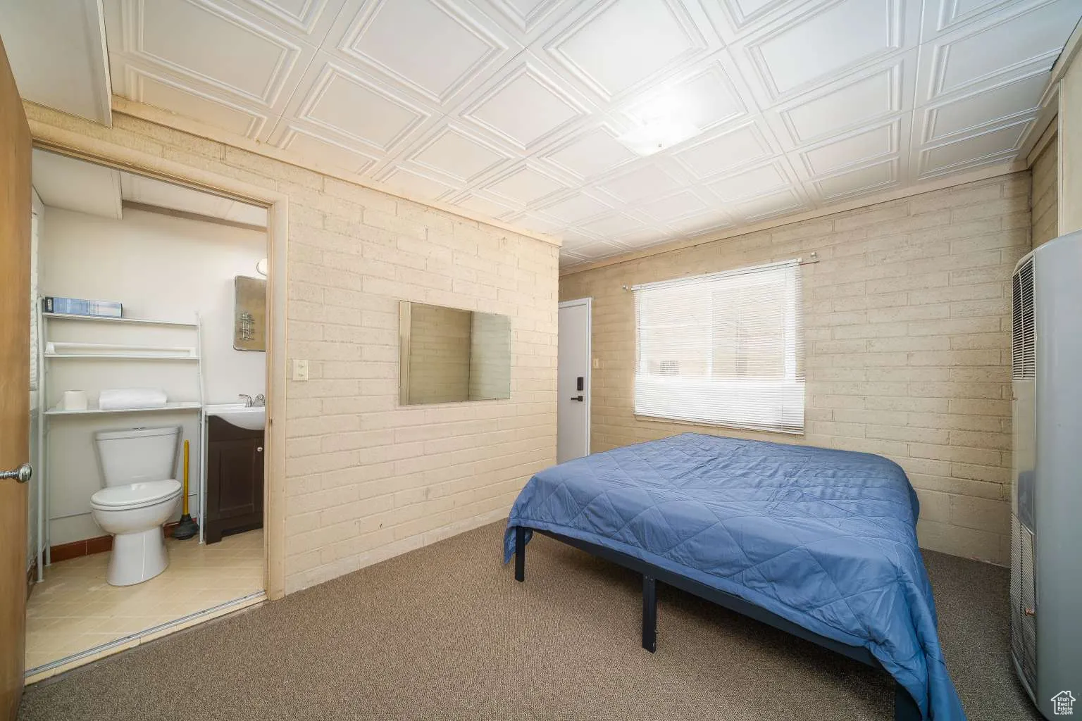 Carpeted bedroom featuring brick wall, a heating unit, ensuite bathroom, and an ornate ceiling