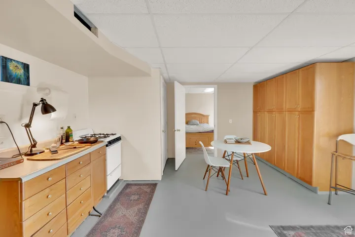 Kitchen with white range with gas stovetop, a drop ceiling, finished concrete floors, and light countertops