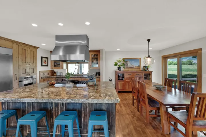 Kitchen featuring wall chimney exhaust hood, recessed lighting, wood finished floors, glass insert cabinets, and appliances with stainless steel finishes