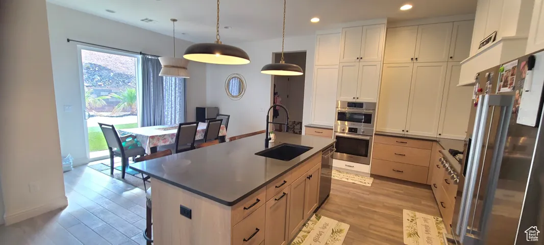 Kitchen featuring a center island with sink, stainless steel appliances, hanging light fixtures, light wood finished floors, and recessed lighting