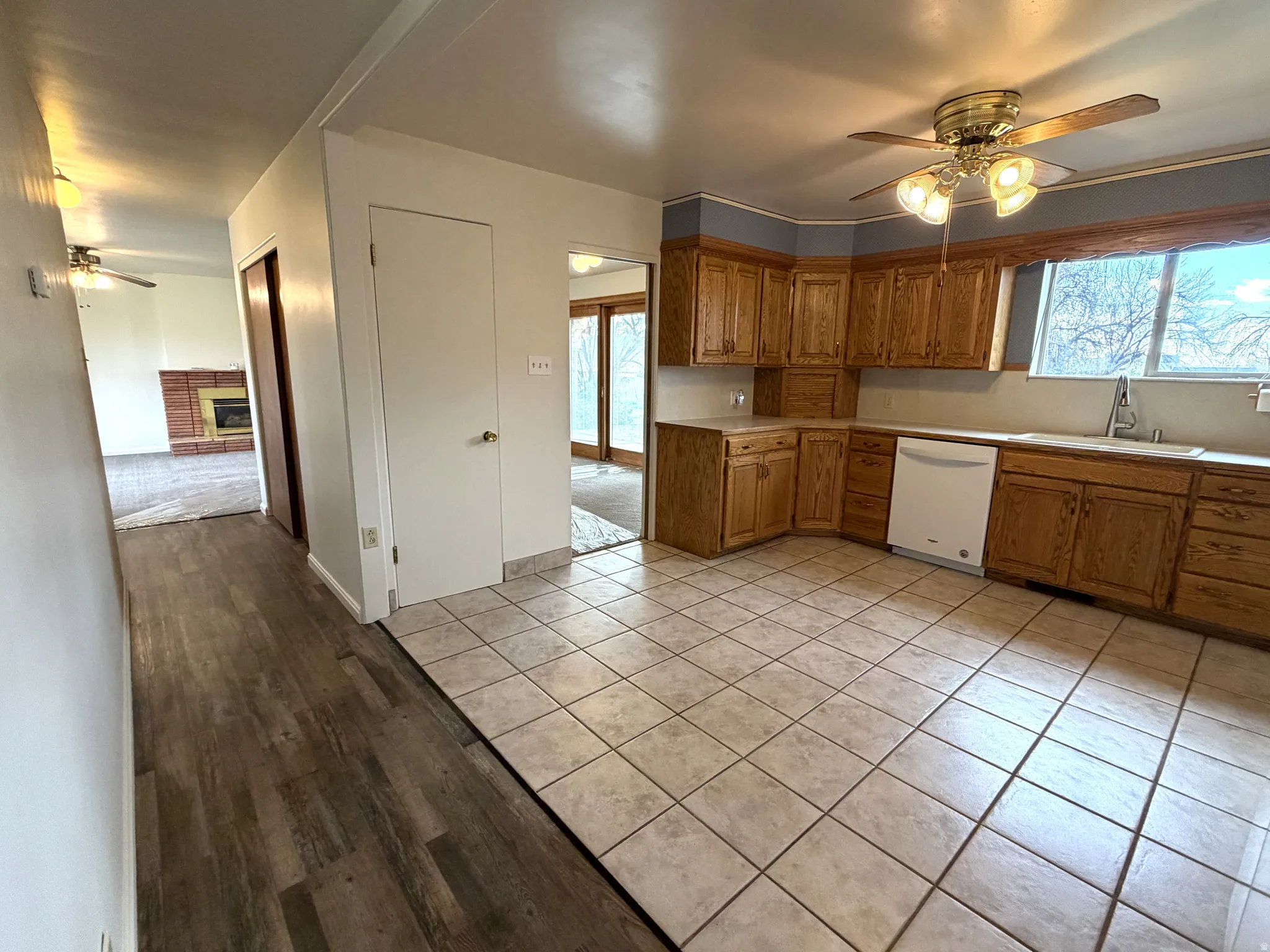 Kitchen featuring a ceiling fan, wood finish cabinets, light tile patterned flooring, light countertops, and dishwasher