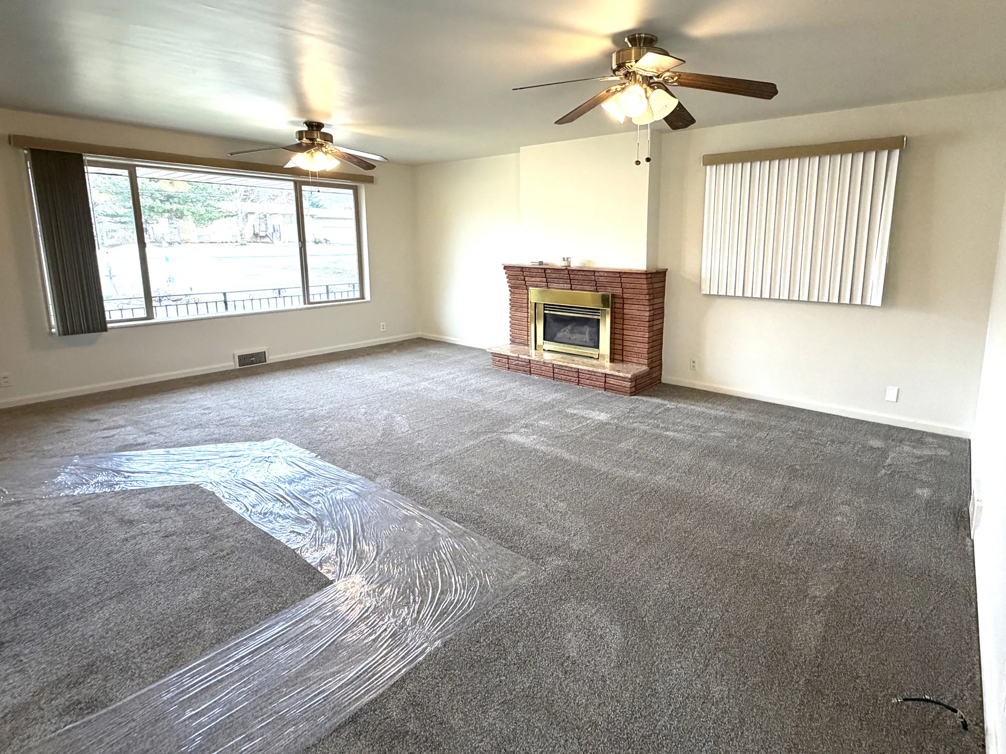 Unfurnished living room featuring a ceiling fan, carpet, and a brick fireplace