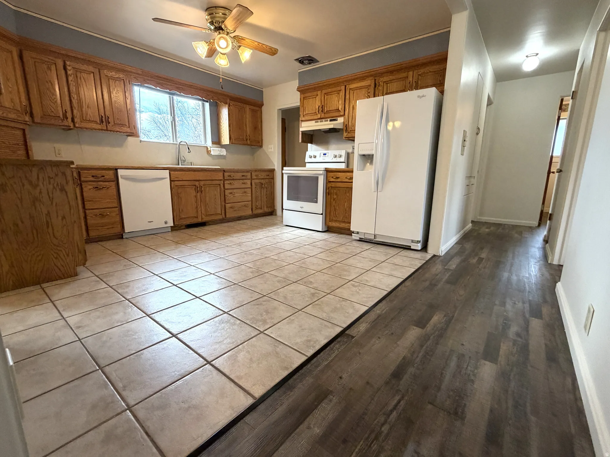 Kitchen featuring white appliances, ceiling fan, wood finish cabinets, light tile patterned flooring, and light countertops