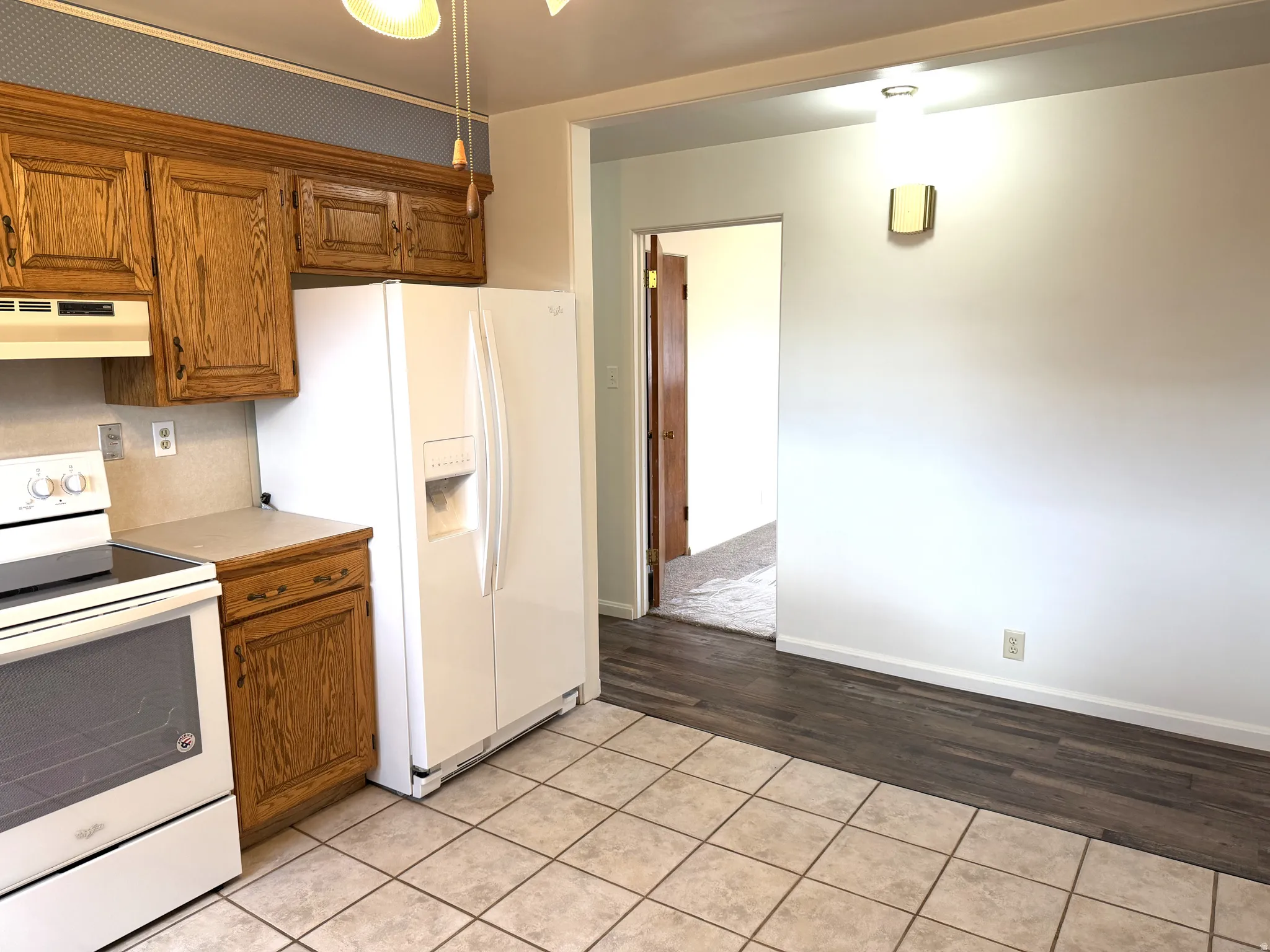 Kitchen featuring wood finish cabinetry, white appliances, light countertops, and light tile patterned floors