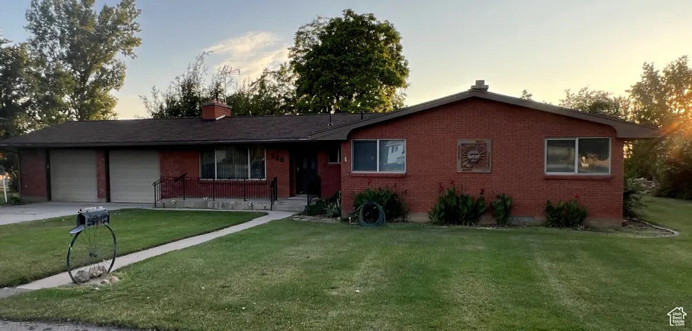 Ranch-style home featuring a chimney, a garage, brick siding, a front yard, and driveway