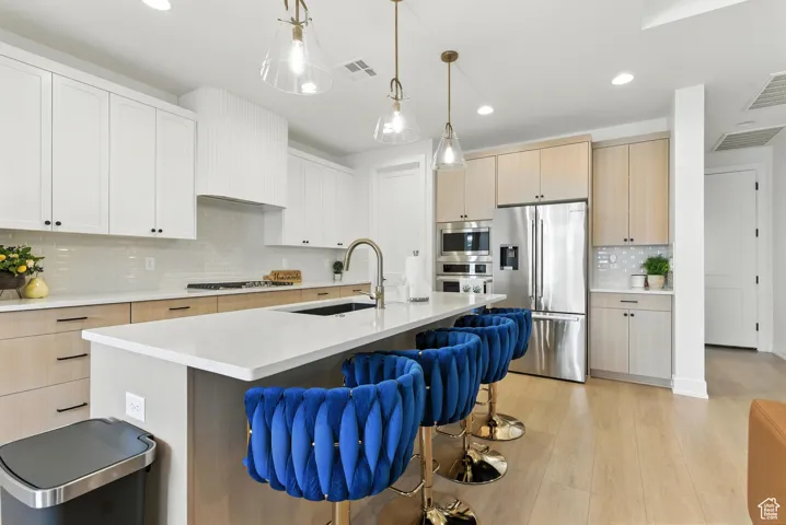 Kitchen featuring stainless steel appliances, tasteful backsplash, a kitchen bar, light countertops, and light wood-style floors