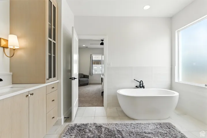 Full bath featuring plenty of natural light, a freestanding tub, tile patterned floors, vanity, and tile walls
