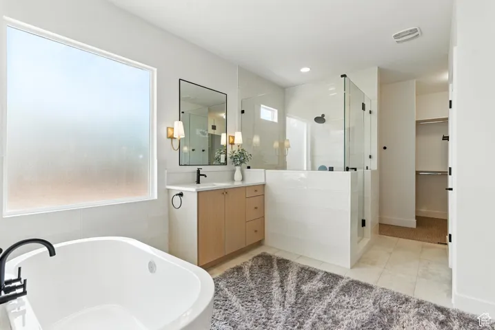 Full bath with a shower stall, vanity, a freestanding bath, tile patterned flooring, and a walk in closet