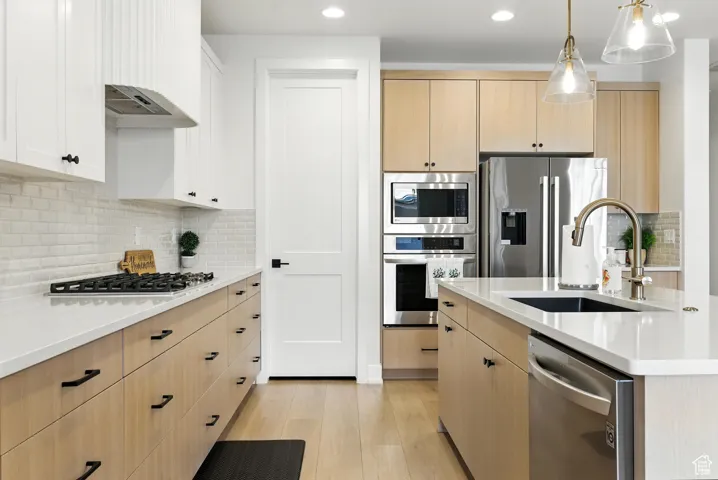 Kitchen with light brown cabinets, stainless steel appliances, light countertops, light wood finished floors, and backsplash