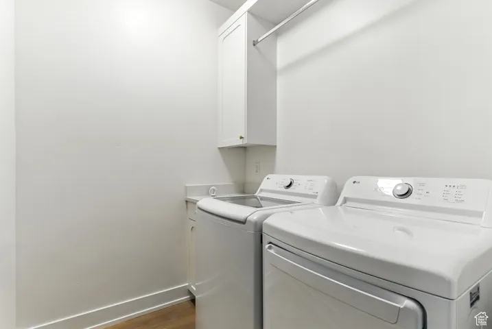 Laundry area featuring washing machine and dryer, cabinet space, and dark wood-style flooring