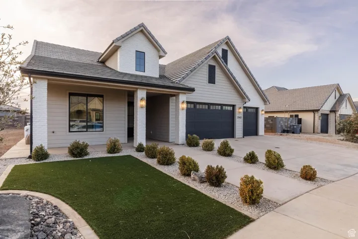 View of front of house with covered porch, brick siding, a front yard, concrete driveway, and an attached garage