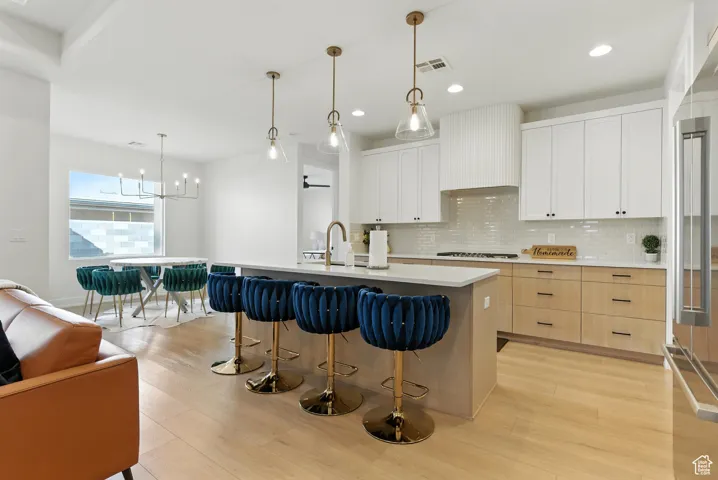 Kitchen with light wood finished floors, decorative backsplash, a breakfast bar area, high end refrigerator, and recessed lighting