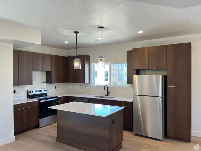 Kitchen featuring stainless steel appliances, light wood-type flooring, light countertops, a kitchen island, and recessed lighting