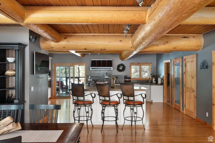 Kitchen featuring dark countertops, a wooden ceiling with exposed beams, wood finished floors, healthy amount of natural light, and a breakfast bar