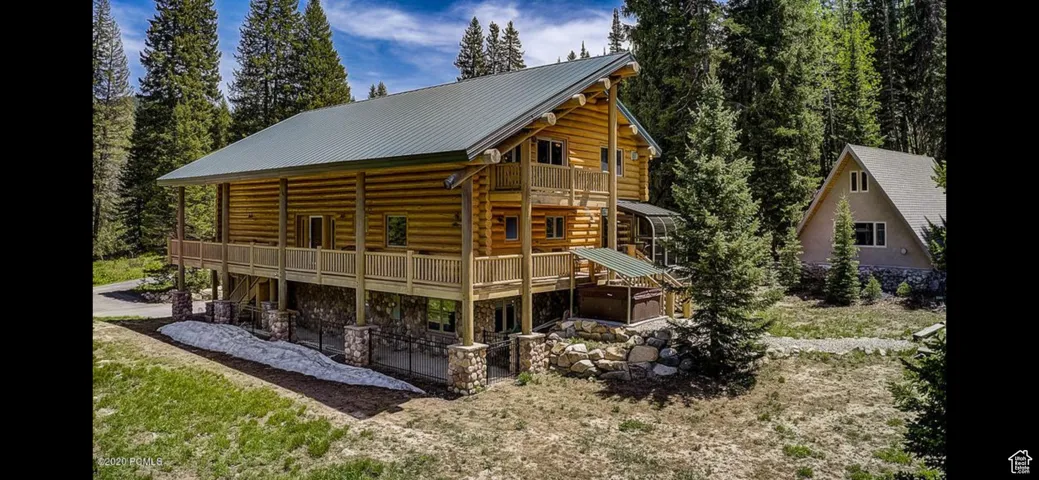 Rear view of house with a patio area, a metal roof, log exterior, stone siding, and a balcony
