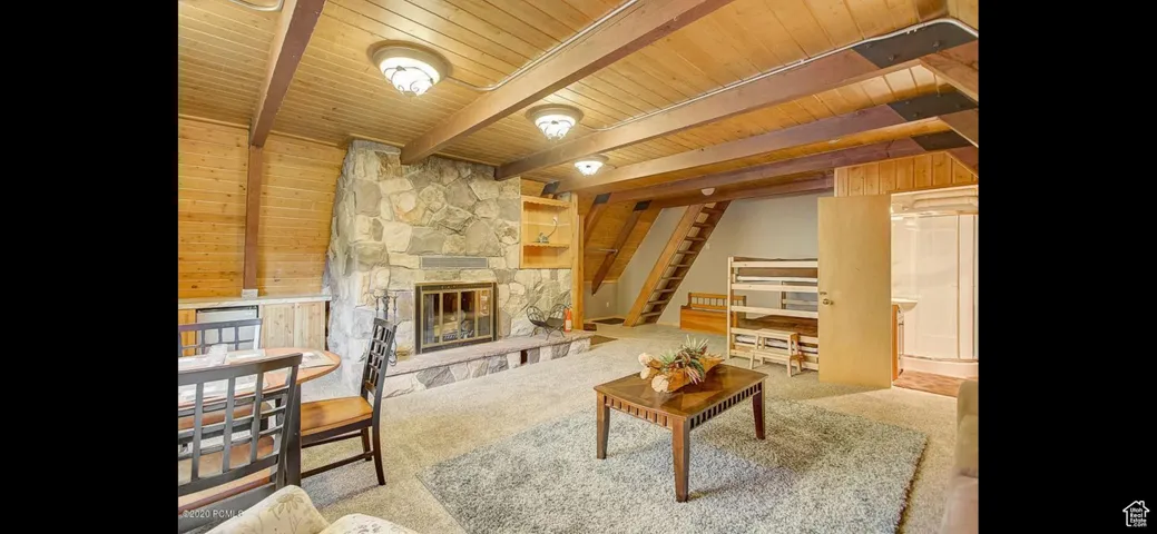 Living room with a wooden ceiling with exposed beams, a stone fireplace, stairway, and wooden walls