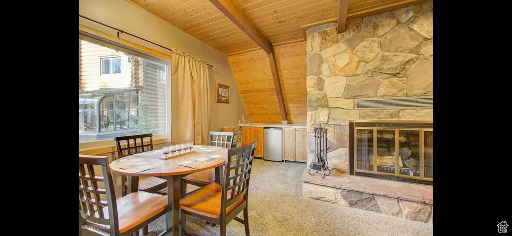 Dining space featuring wood ceiling, a stone fireplace, and carpet flooring