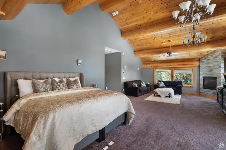 Carpeted bedroom with a chandelier, high vaulted ceiling, a wooden ceiling with exposed beams, and a fireplace
