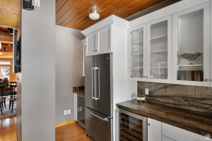 Kitchen with high quality fridge, wine cooler, light wood-style floors, wooden ceiling, and glass insert cabinets