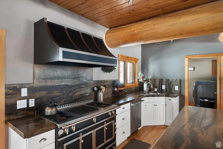 Kitchen with a wood ceiling with exposed beams, custom range hood, black electric range, white cabinets, and decorative backsplash
