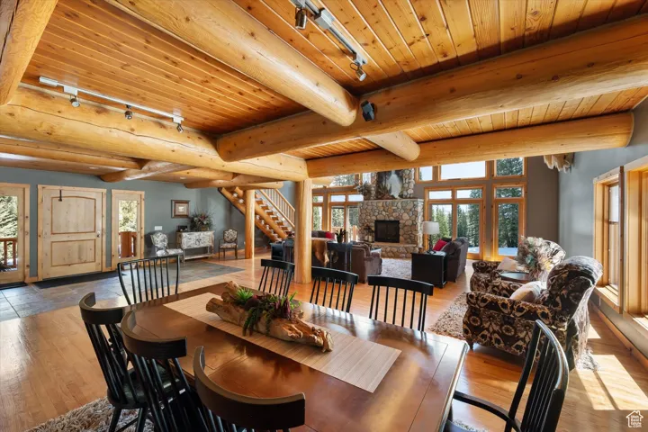 Dining room featuring a wooden ceiling with exposed beams, hardwood / wood-style flooring, a stone fireplace, rail lighting, and stairway